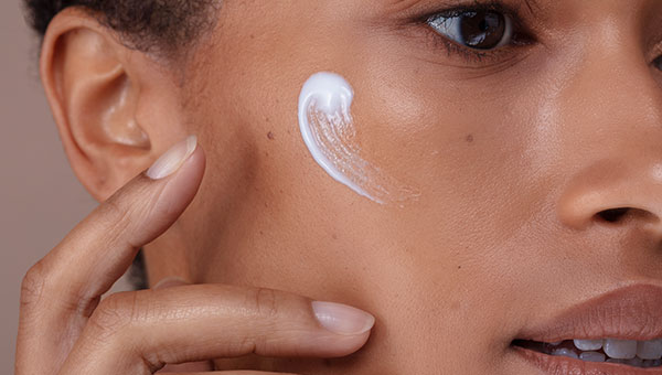 Close-Up von Frau die Creme aufträgt und in die Kamera lächelt