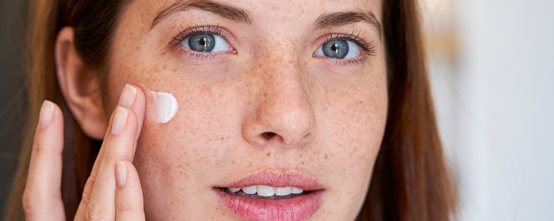 Junge Frau mit Sommersprossen trägt Gesichtscreme auf