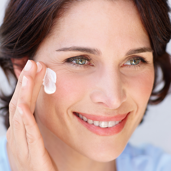 Lächelnde Frau trägt sanft Gesichtscreme auf die Wange auf